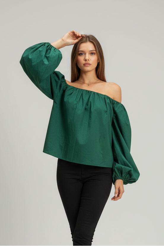 Woman wearing a green off-shoulder blouse with black pants on a gray background