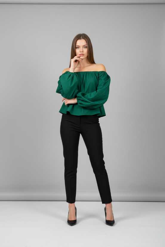 Woman wearing a green off-shoulder top and black pants against a gray background